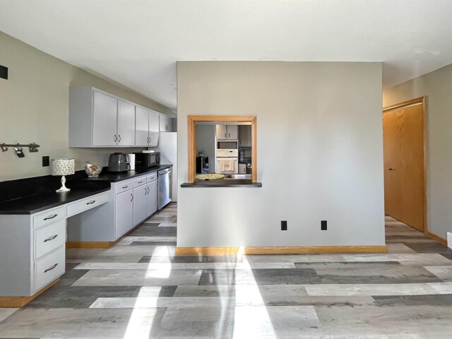 kitchen with black microwave, dark countertops, stainless steel dishwasher, baseboards, and light wood-style flooring