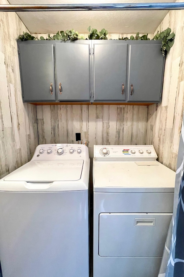 laundry area featuring wooden walls, independent washer and dryer, and cabinet space