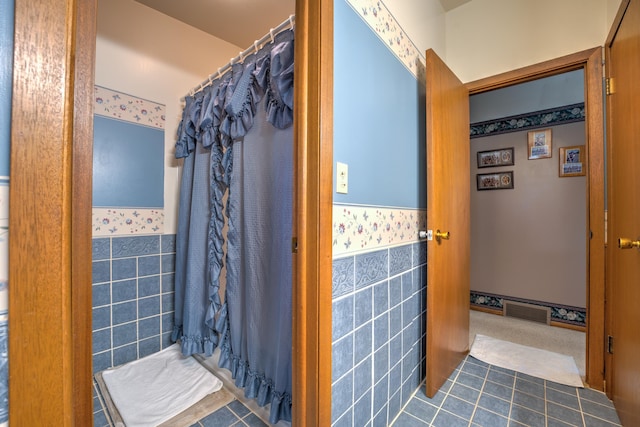 bathroom with a shower with curtain, visible vents, tile walls, tile patterned flooring, and wainscoting