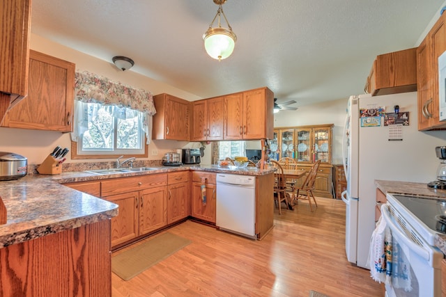 kitchen featuring a peninsula, white appliances, ceiling fan, a sink, and light wood finished floors