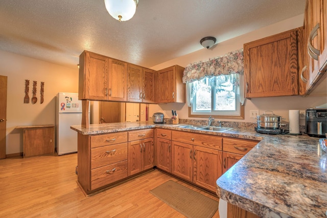 kitchen with brown cabinetry, a sink, freestanding refrigerator, light wood finished floors, and a peninsula