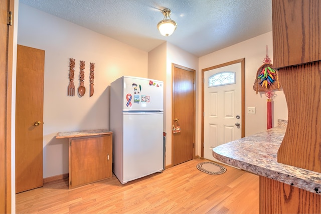 kitchen with light countertops, freestanding refrigerator, light wood-type flooring, and a textured ceiling