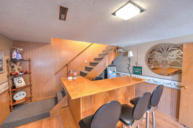 bar with a textured ceiling, stairs, wood finished floors, and wood walls
