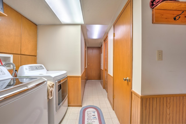 washroom with laundry area, washing machine and clothes dryer, wood walls, light tile patterned floors, and a wainscoted wall