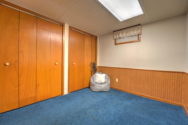 unfurnished bedroom with carpet flooring, multiple closets, a wainscoted wall, and a paneled ceiling