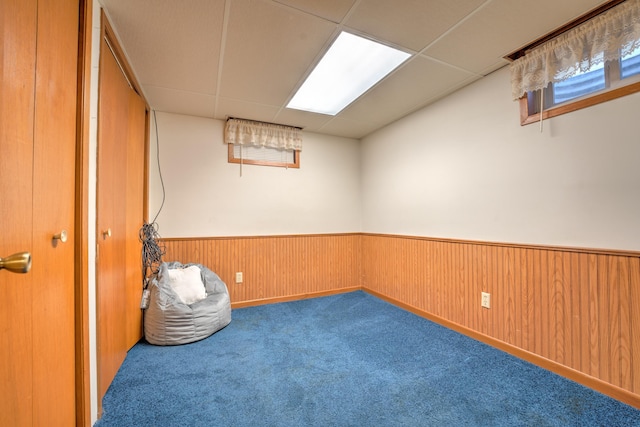 below grade area with carpet flooring, wainscoting, and a drop ceiling