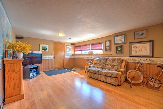 living area with a textured ceiling, wood walls, wood finished floors, and a wainscoted wall