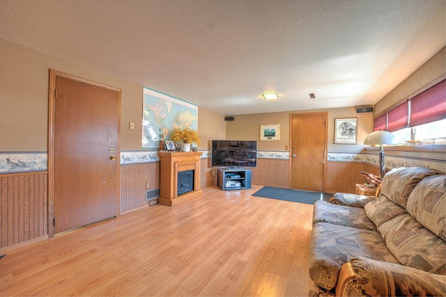 living area with a wainscoted wall, a textured ceiling, and light wood-style flooring