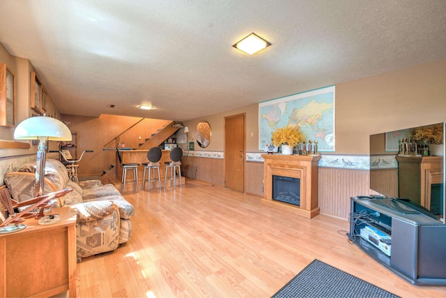 living area with wainscoting, a textured ceiling, a glass covered fireplace, wood finished floors, and stairway
