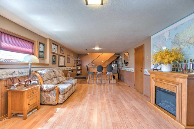 living area featuring light wood-style floors, a wainscoted wall, wood walls, and a textured ceiling