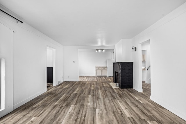 unfurnished living room with a brick fireplace, baseboards, and dark wood finished floors
