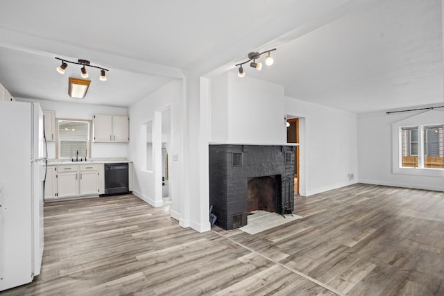 unfurnished living room with a fireplace, rail lighting, light wood-type flooring, visible vents, and baseboards