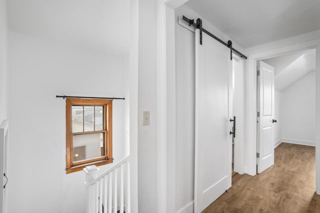 hallway featuring baseboards, vaulted ceiling, a barn door, and wood finished floors
