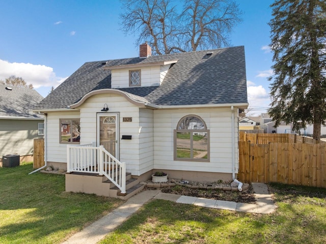 bungalow-style house with fence, central AC, a front yard, a chimney, and a shingled roof