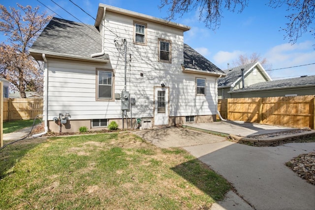 back of property featuring roof with shingles, a patio area, fence, and a lawn