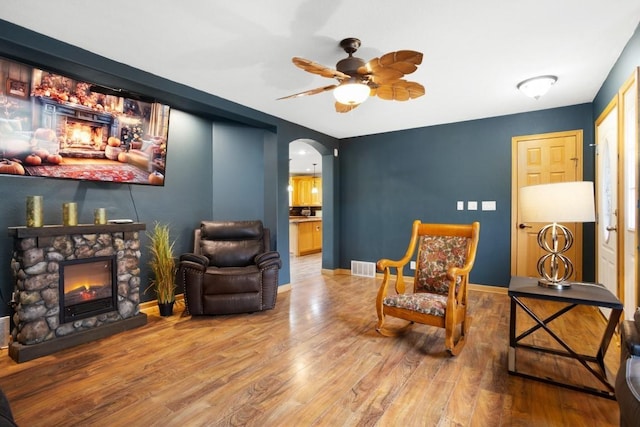 living area with wood finished floors, visible vents, a fireplace, arched walkways, and a ceiling fan