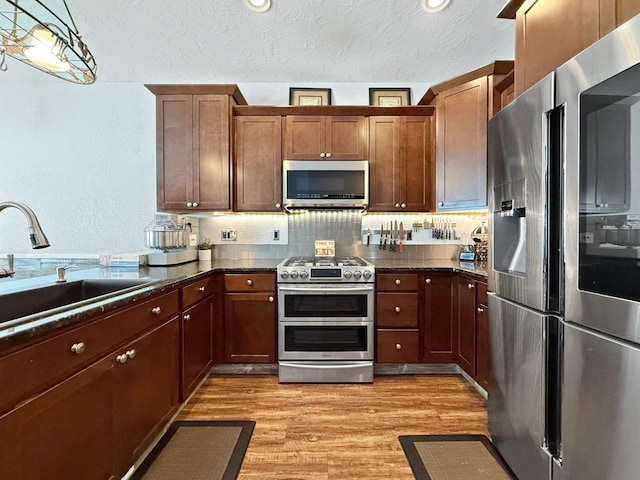4005 Crossing St, Minot, ND 58701 - kitchen featuring light wood-style flooring, dark stone countertops, a sink, a textured ceiling, and appliances with stainless steel finishes