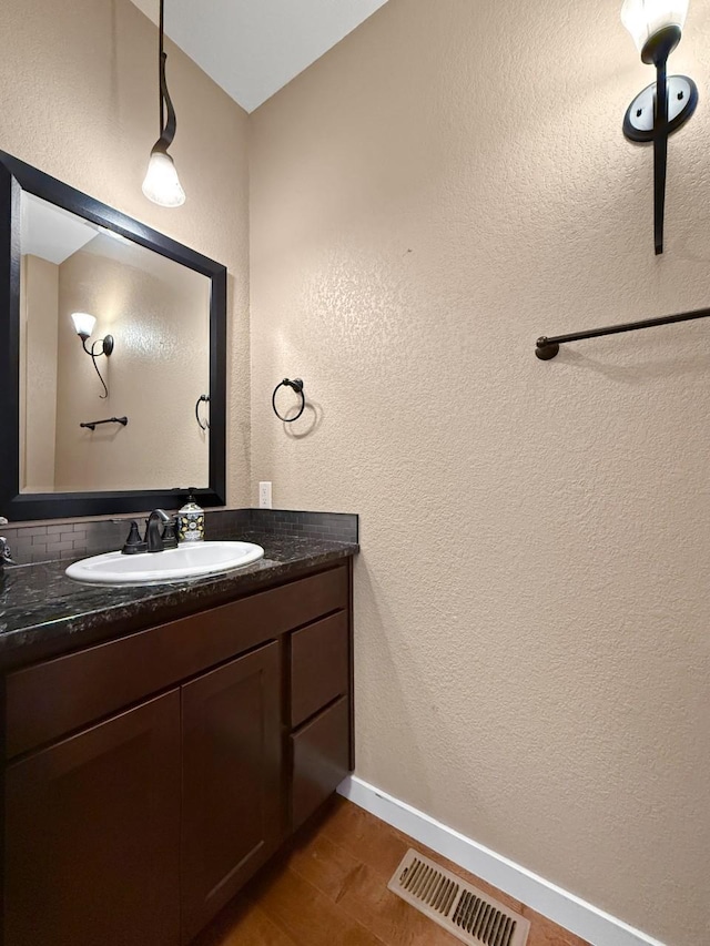 4005 Crossing St, Minot, ND 58701 - bathroom with wood finished floors, vanity, visible vents, a textured wall, and baseboards