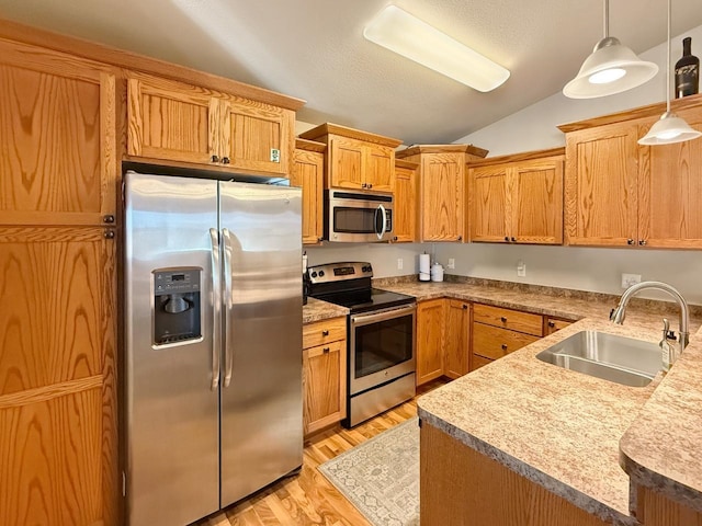 kitchen featuring hanging light fixtures, light wood-style flooring, a sink, appliances with stainless steel finishes, and vaulted ceiling