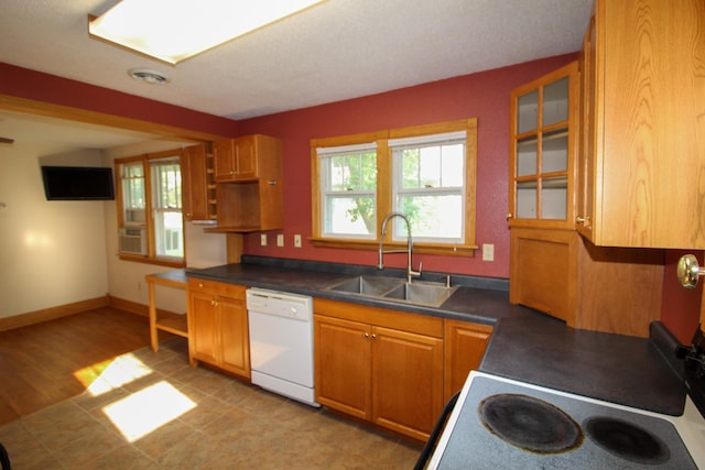 kitchen with a sink, plenty of natural light, dark countertops, and white dishwasher