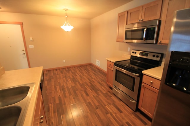 kitchen with stainless steel appliances, dark wood-type flooring, a sink, light countertops, and hanging light fixtures