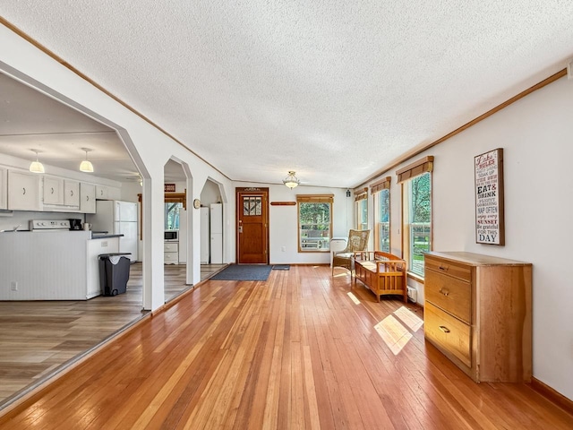 living area featuring a textured ceiling, arched walkways, ceiling fan, light wood-style floors, and baseboards