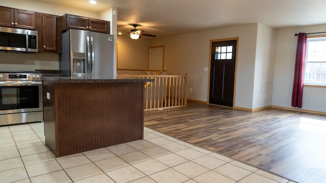 611 16th St, Minot, ND 58701 - kitchen featuring appliances with stainless steel finishes, light tile patterned floors, a ceiling fan, a center island, and dark brown cabinetry
