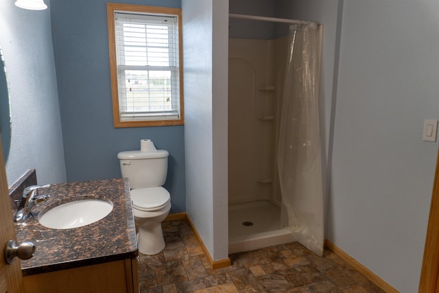 611 16th St, Minot, ND 58701 - bathroom featuring baseboards, stone finish flooring, a stall shower, vanity, and toilet