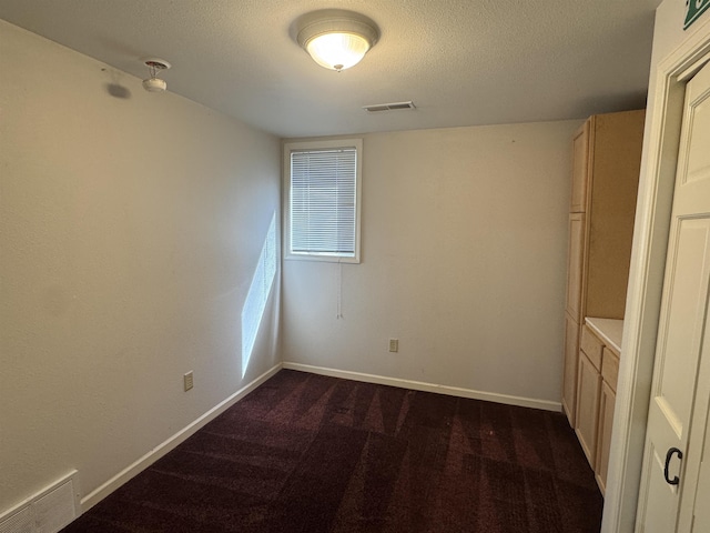 701 9th Ave, Minot, ND 58703 - spare room featuring dark colored carpet, baseboards, and a textured ceiling