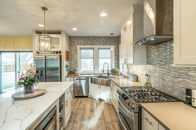 615 2nd St, Garrison, ND 58540 - kitchen with wall chimney exhaust hood, stainless steel appliances, a sink, light wood-style floors, and white cabinets