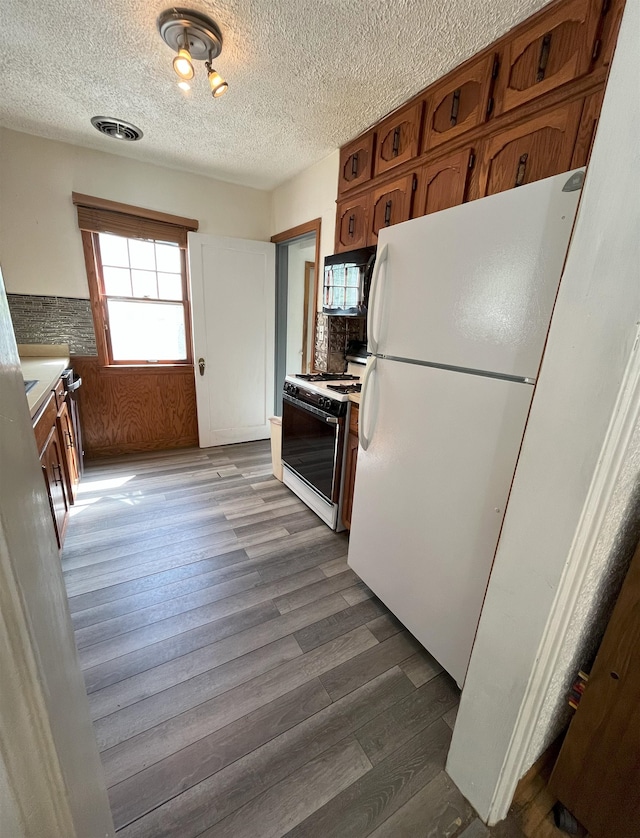 909 NW 10th Ave, Minot, ND 58703 - kitchen with white appliances, a textured ceiling, dark wood finished floors, brown cabinetry, and light countertops