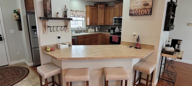1728 Rivers Edge, Minot, ND 58701 - kitchen featuring appliances with stainless steel finishes, a sink, decorative backsplash, a peninsula, and a breakfast bar