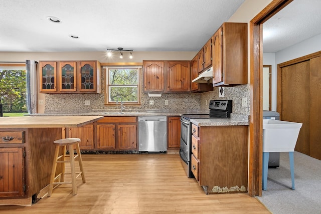 3574 91st St, Mohall, ND 58761 - kitchen featuring stainless steel appliances, brown cabinets, a sink, under cabinet range hood, and decorative backsplash