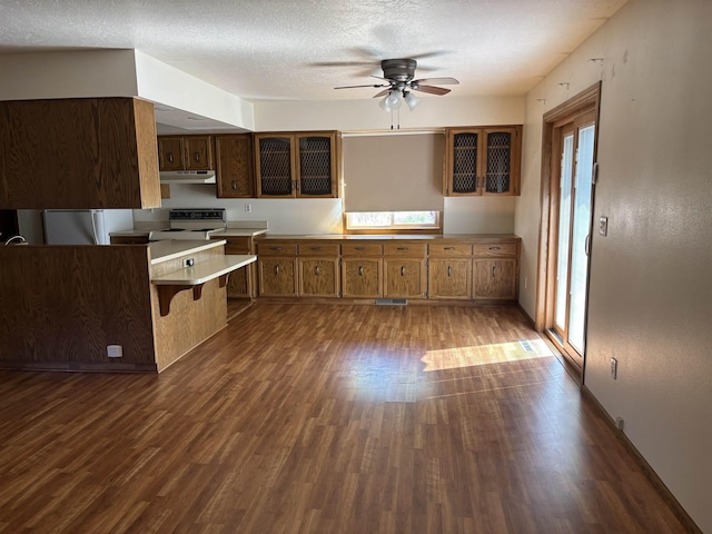 2420 8th St Unit 2420, Minot, ND 58703 - kitchen featuring dark wood-style flooring, a ceiling fan, brown cabinets, a kitchen breakfast bar, and range with electric stovetop