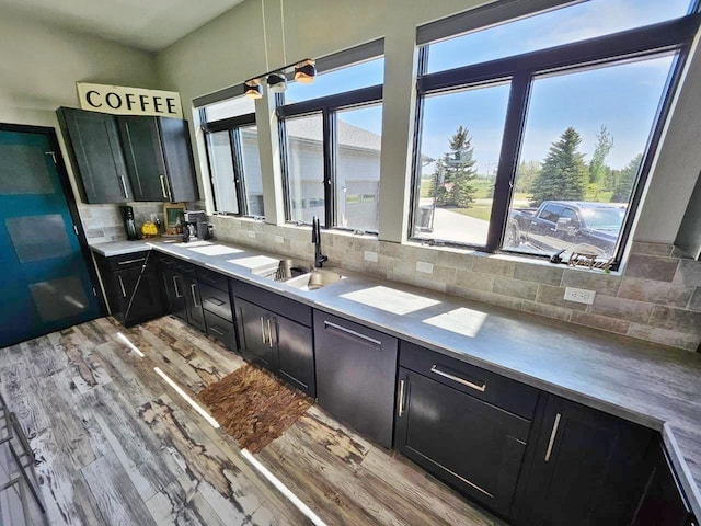 1007 5th St, Rugby, ND 58368 - kitchen featuring dark cabinetry, a sink, light wood-type flooring, backsplash, and light countertops