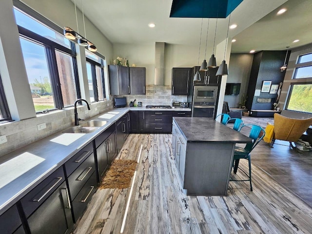 1007 5th St, Rugby, ND 58368 - kitchen featuring wall chimney exhaust hood, a sink, light wood-style floors, a center island, and backsplash
