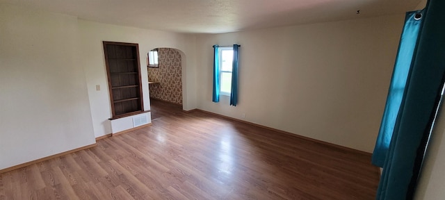 101 Central Ave, Des Lacs, ND 58733 - spare room with arched walkways, wood finished floors, and baseboards