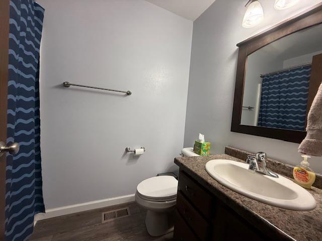1805 28th St, Minot, ND 58703 - bathroom with wood finished floors, baseboards, vanity, toilet, and curtained shower