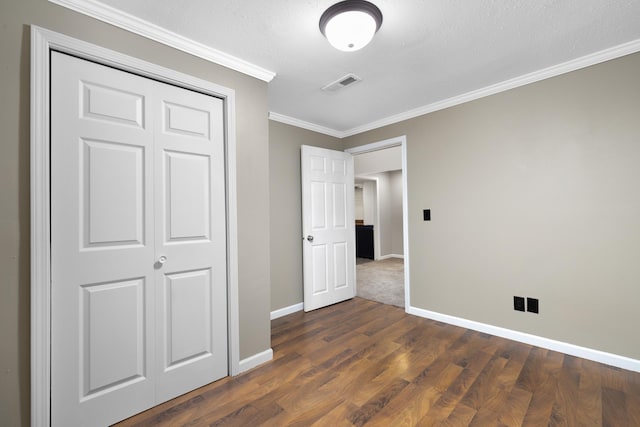 1111 15th St, Minot, ND 58703 - unfurnished bedroom with baseboards, crown molding, dark wood-style flooring, and a closet
