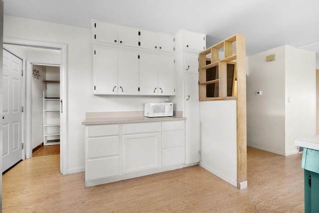 1200 9th St, Minot, ND 58703 - kitchen featuring light wood-style flooring, white microwave, white cabinetry, light countertops, and baseboards