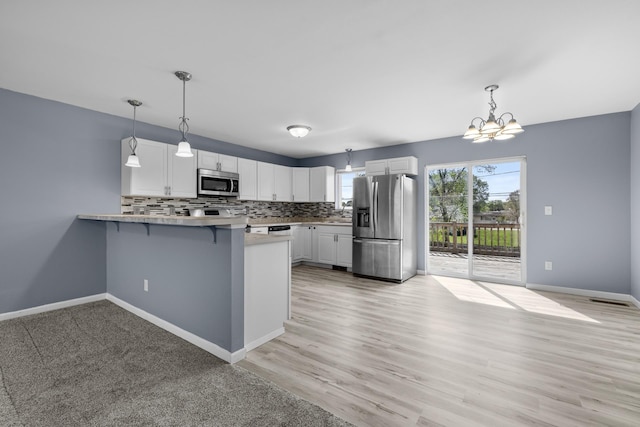 205 17th St, Minot, ND 58703 - kitchen featuring stainless steel appliances, a peninsula, a chandelier, white cabinets, and baseboards