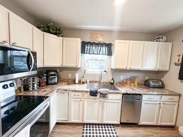 101 6th St, Minot, ND 58703 - kitchen featuring stainless steel appliances, a sink, light wood-type flooring, and white cabinetry