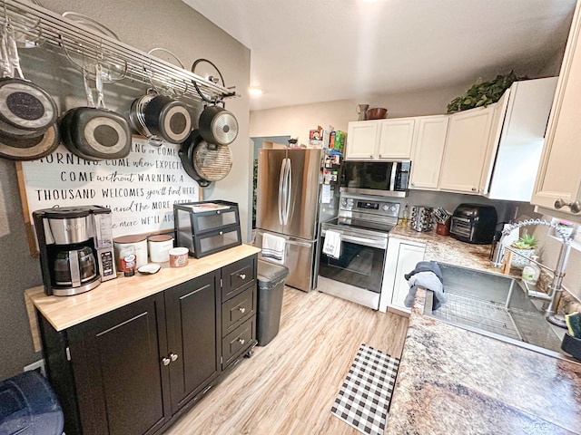101 6th St, Minot, ND 58703 - kitchen with appliances with stainless steel finishes, white cabinets, light countertops, light wood finished floors, and dark cabinetry