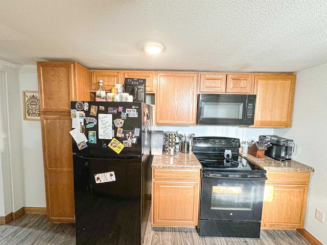 101 6th St, Minot, ND 58703 - kitchen with black appliances, light wood finished floors, baseboards, a textured ceiling, and light stone counters