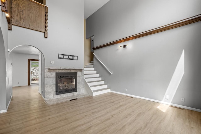 1127 8th St, Minot, ND 58703 - unfurnished living room featuring wood finished floors, a tiled fireplace, arched walkways, baseboards, and a towering ceiling