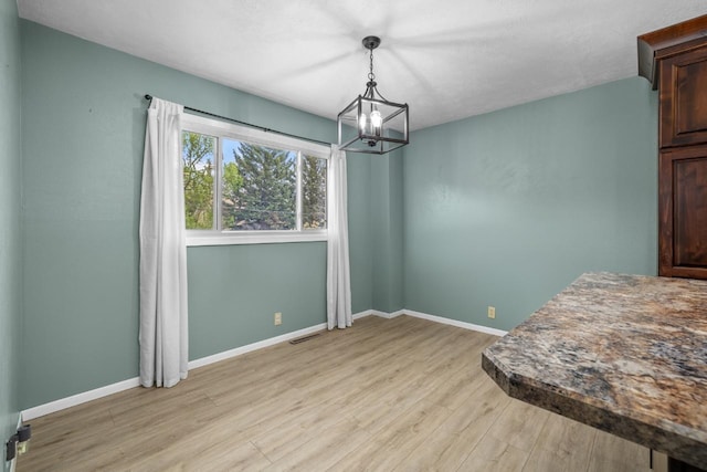 1127 8th St, Minot, ND 58703 - unfurnished dining area with a chandelier, light wood-style flooring, and baseboards