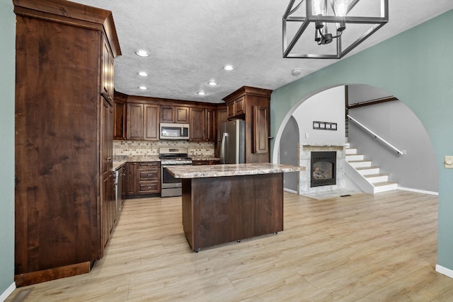 1127 8th St, Minot, ND 58703 - kitchen with appliances with stainless steel finishes, arched walkways, recessed lighting, a glass covered fireplace, and tasteful backsplash