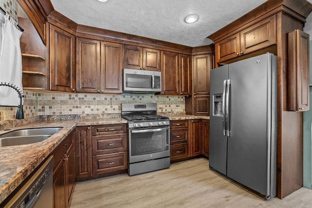 1127 8th St, Minot, ND 58703 - kitchen with stainless steel appliances, a sink, a textured ceiling, light wood finished floors, and backsplash