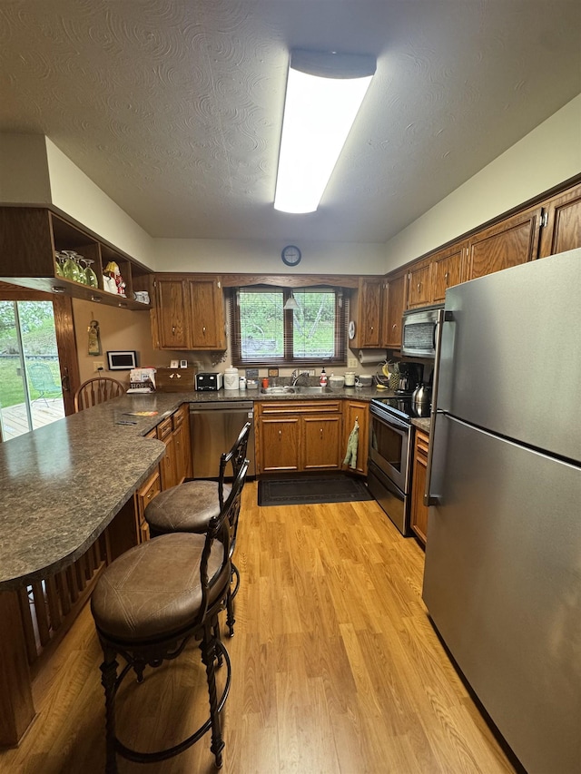1130 8th St, Minot, ND 58703 - kitchen featuring appliances with stainless steel finishes, a sink, dark countertops, light wood-style floors, and brown cabinets