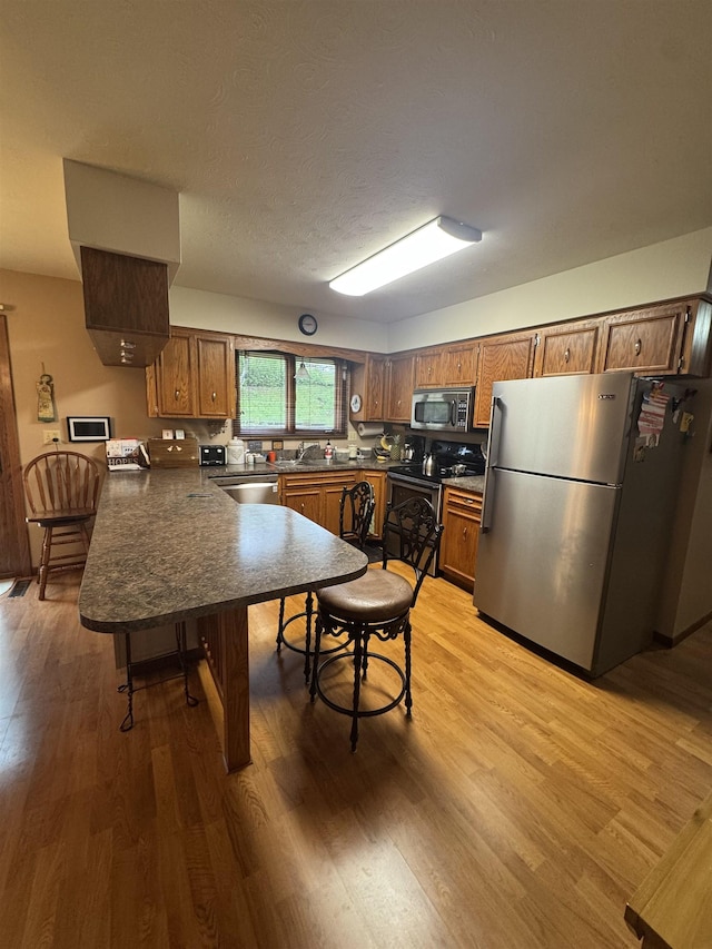 1130 8th St, Minot, ND 58703 - kitchen with stainless steel appliances, a peninsula, dark countertops, light wood-style flooring, and brown cabinetry